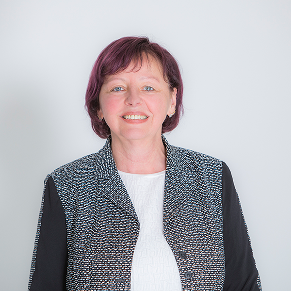 Portrait of a smiling woman with short purple hair, wearing a black-and-white patterned blazer over a white blouse.