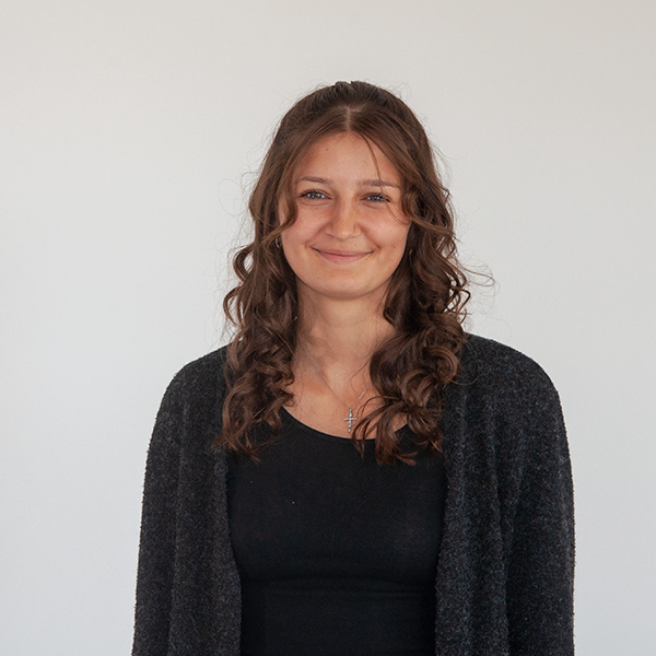 Smiling woman with curly brown hair wearing a black top and gray cardigan against a light gray background.