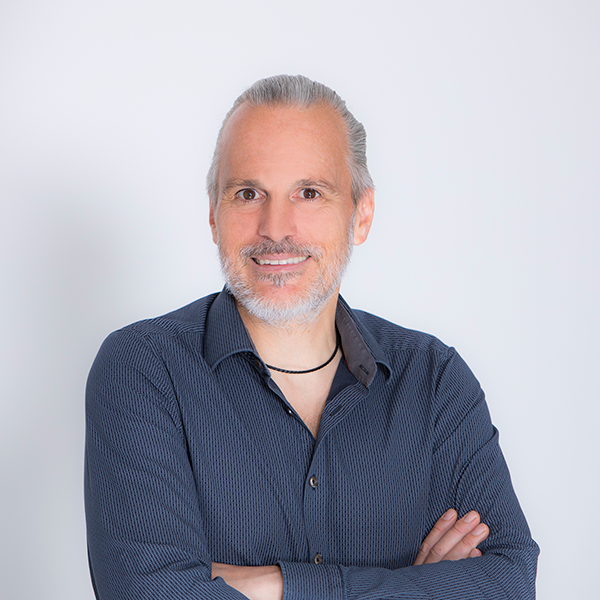 Smiling middle-aged man with gray hair and beard, wearing a dark blue button-up shirt, arms crossed.