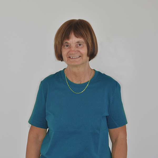 Smiling woman in a teal shirt stands against a light gray background.
