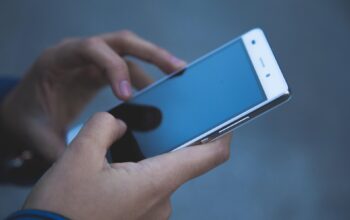 Person holding a smartphone and tapping its screen with both hands, close-up view from the side.