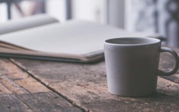 White ceramic coffee mug on a rustic wooden table with an open notebook in the blurred background.