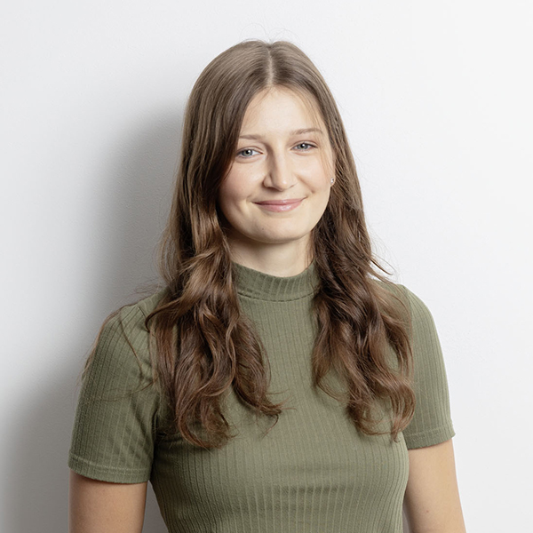 Portrait of a smiling young woman with long brown hair in a green ribbed tee against a light background.