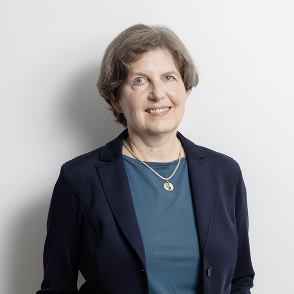 Professional portrait of a smiling middle-aged woman in a navy blazer and teal top, against a light background.