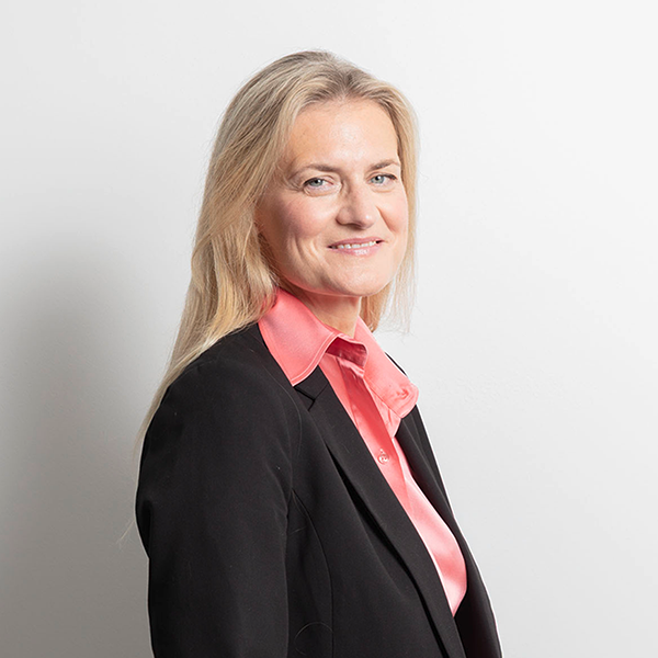 Professional portrait of a smiling blonde woman wearing a black blazer and pink shirt against a white background