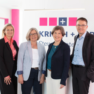 Four professionals posing for a photo in an office, standing in front of a sign with a blue cross logo.