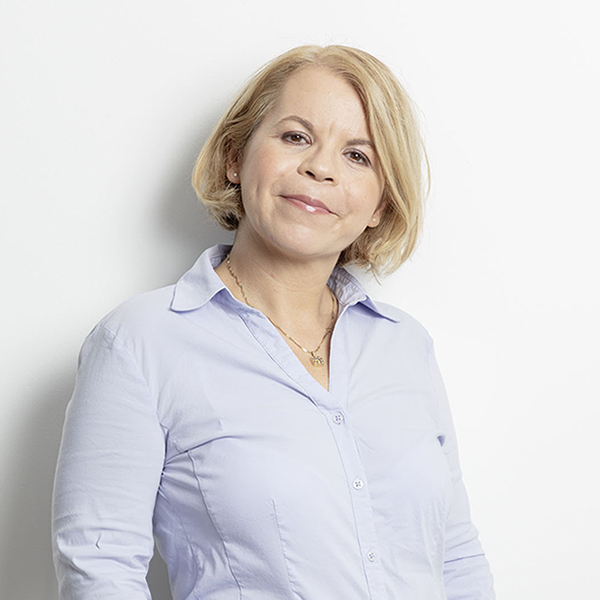 Portrait of a smiling woman with short blonde hair wearing a light blue button-down shirt against a white background.